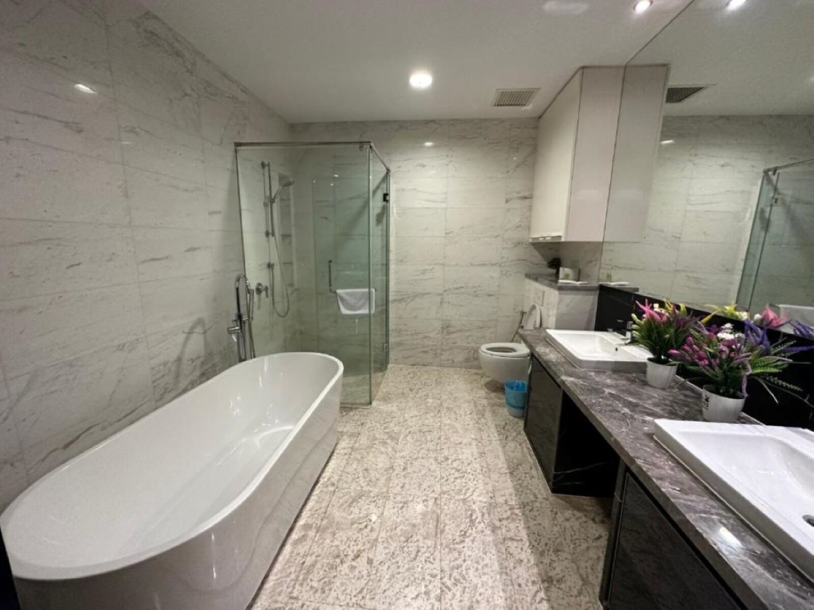 Un baño moderno con una bañera independiente, ducha con mampara de vidrio y tocador con lavamanos y espejo.