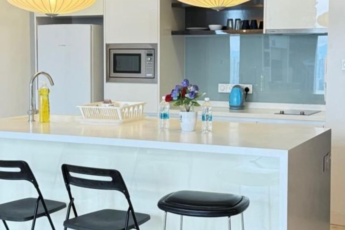 Una cucina moderna con un'isola centrale, due sedie nere, un forno a microonde e un bollitore.