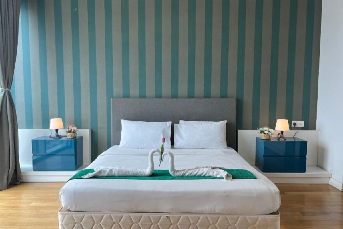 Cama decorada com um cisne, duas mesas de cabeceira com luminárias e parede listrada.