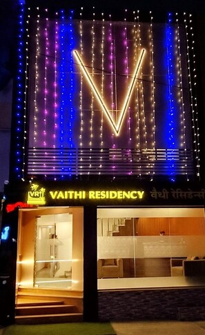 Un edificio con un neon che riporta la scritta "VAITHI RESIDENCY" e un interno moderno con una scala e una zona salotto.