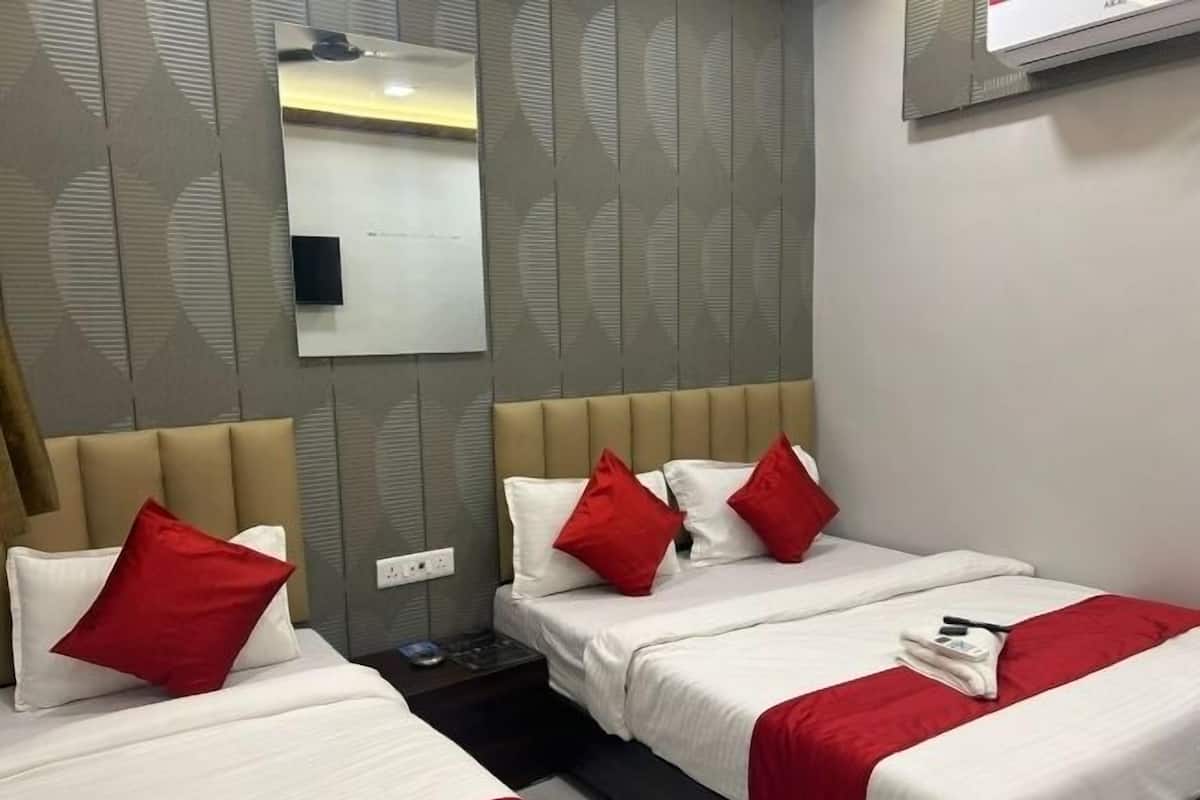 Une chambre d’hôtel avec deux lits, chacun étant équipé de draps blancs et d’oreillers rouges. Une petite table se trouve entre les lits, et un climatiseur mural est fixé au-dessus des lits.