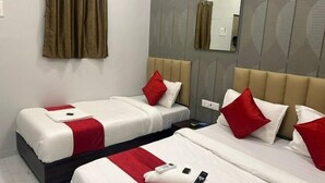 Hotellihuone, jossa on kaksi sänkyä, molemmissa valkoiset lakanat ja punaiset tyynyt, suuri peili ja kuviollinen seinä.