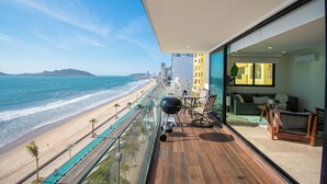 Un balcon avec vue sur la plage et l’océan, un coin salon avec une table et des chaises, et un intérieur moderne avec un canapé et une plante.