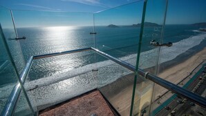 Une pièce aux murs de verre offrant une vue sur l’océan et une plage.