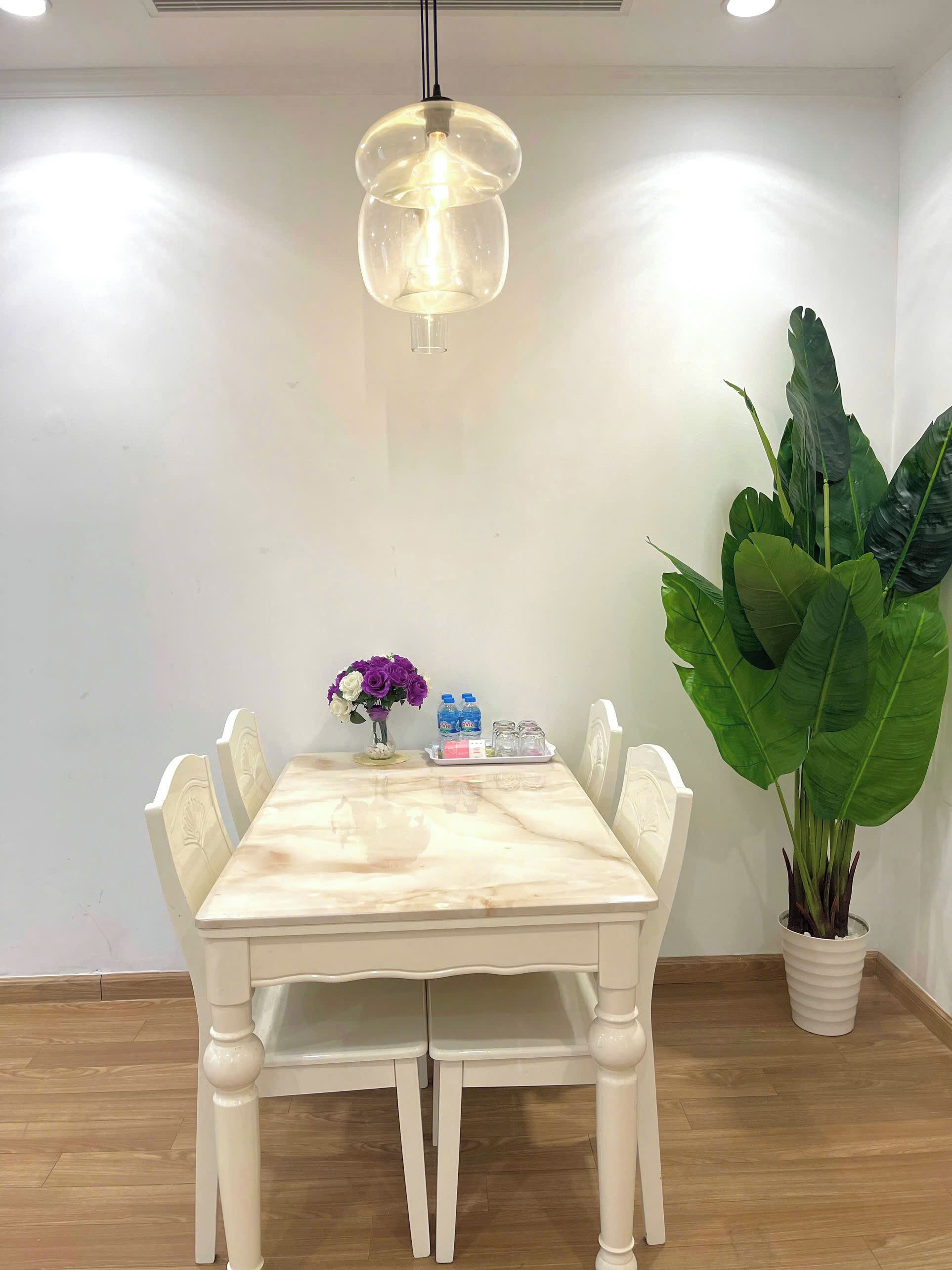 A dining area with a marble table, white chairs, a potted plant, and a pendant light.