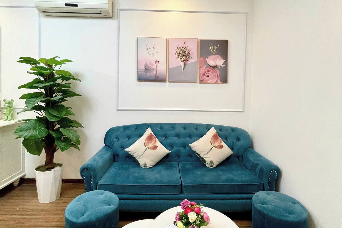 Ein modernes Wohnzimmer mit einem türkisfarbenen Sofa, zwei passenden Poufs, einem weißen Couchtisch mit Blumenvase und einer Wand-Klimaanlage.