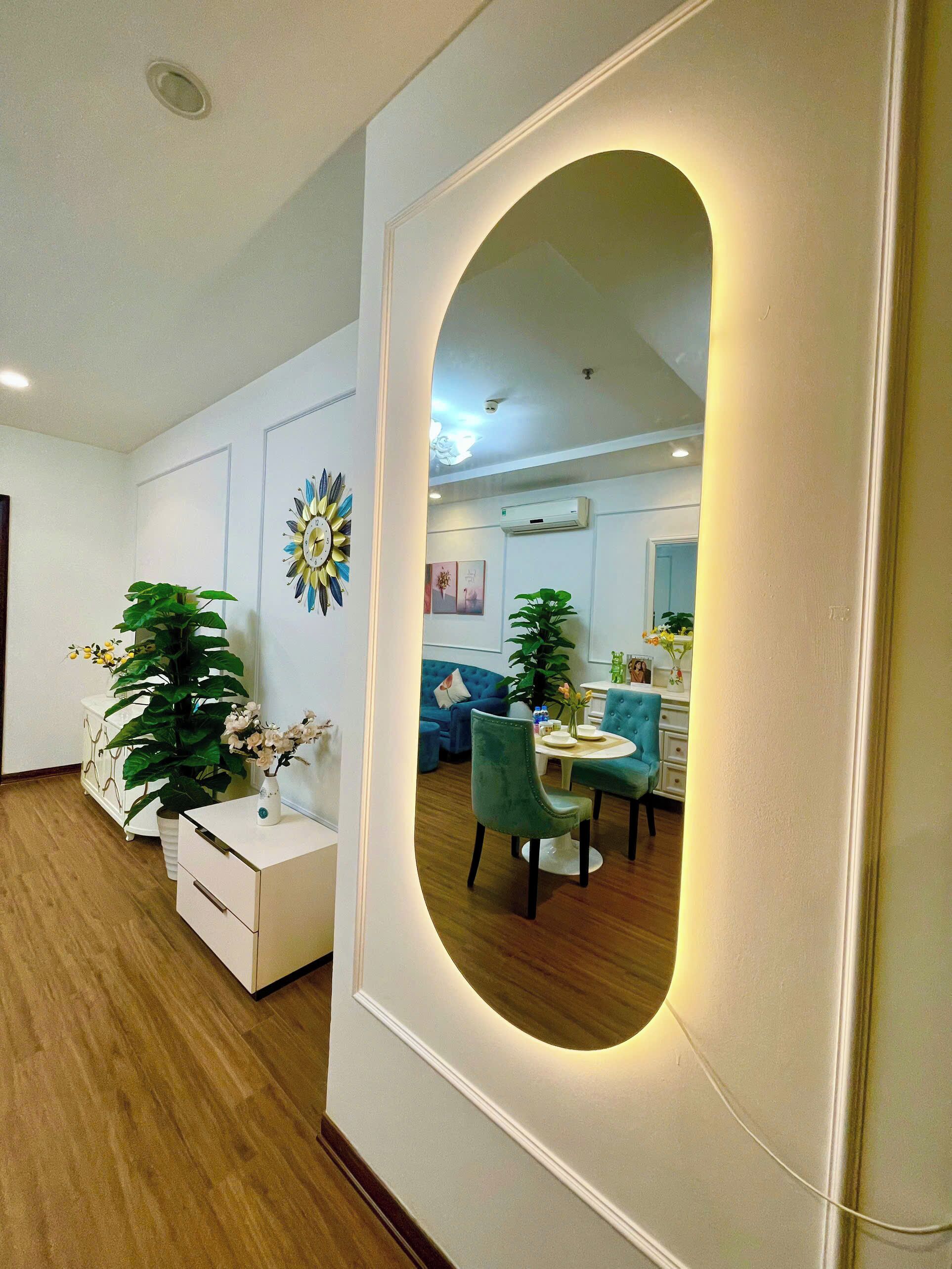 A modern interior with a large oval mirror, white furniture, and green chairs.