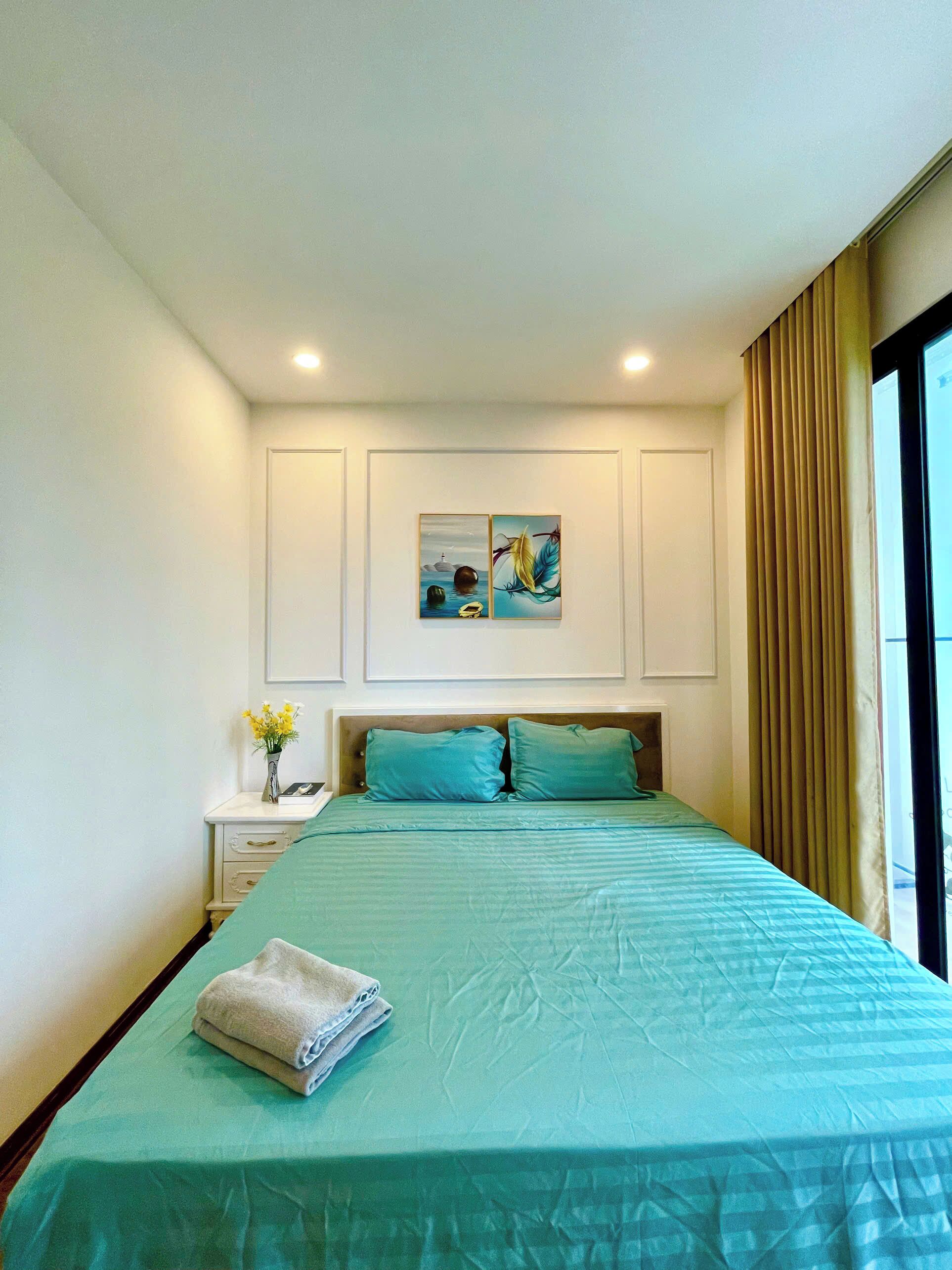 Une chambre d’hôtel avec un lit, une table de chevet, un vase de fleurs et un tableau au mur.
