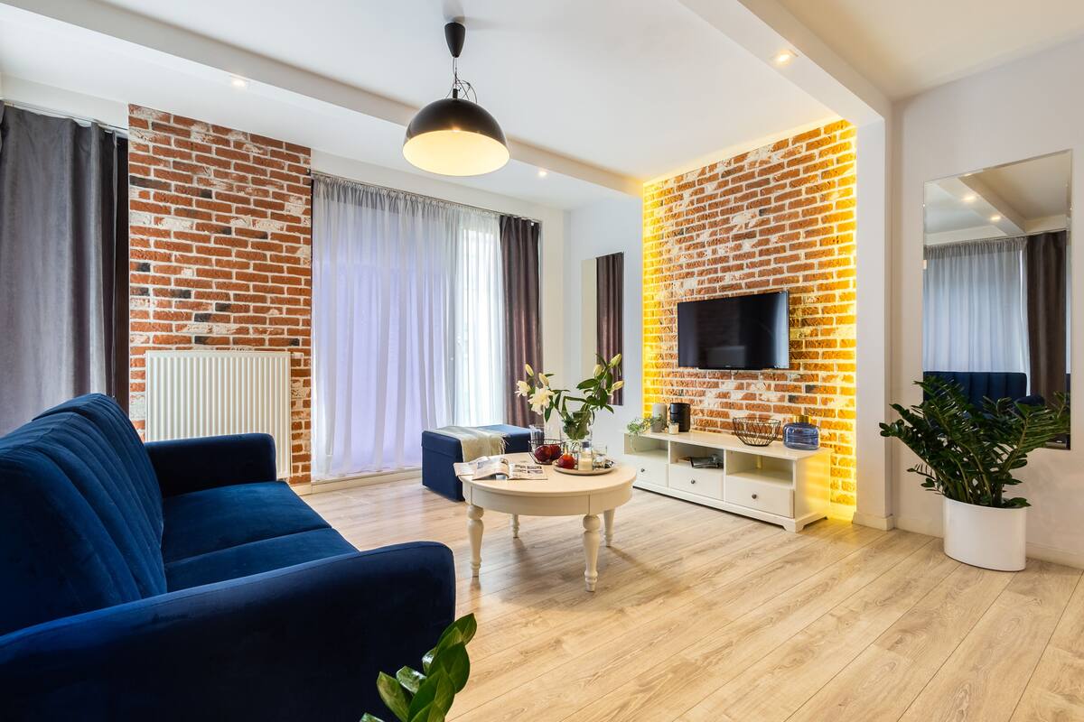 A modern living room with a blue sofa, a round coffee table, a TV, and a brick wall accent.