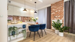 A modern kitchen with white cabinets, a brick accent wall, and a dining area with blue velvet chairs. - Absyntapart Krawiecka - parking w cenie (Wroclaw)