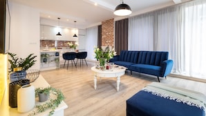 A modern living room with a blue sofa, a round coffee table, and a dining area with a kitchen in the background. - Absyntapart Krawiecka - parking w cenie (Wroclaw)