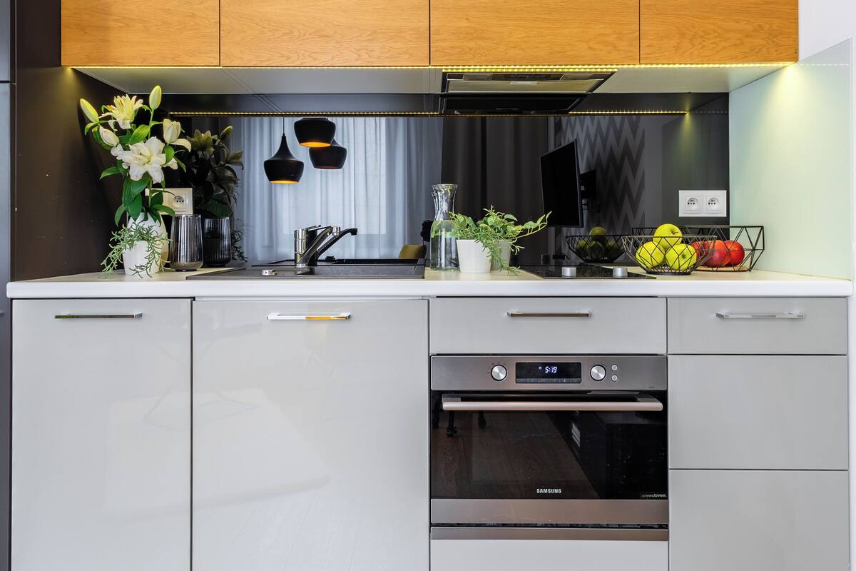 A modern kitchen with wooden cabinets, a stainless steel range hood, a built-in oven, and a sink.
