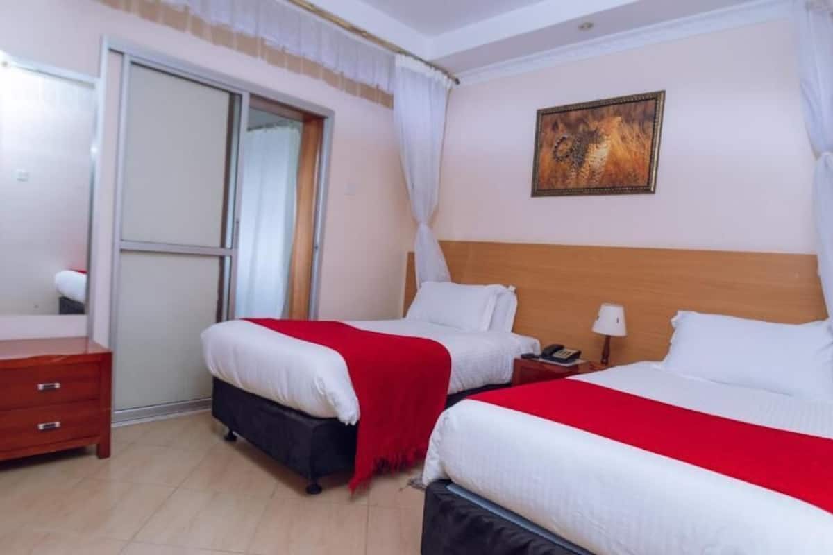 A hotel room with two beds, a wooden nightstand, a mirror, a sliding door, and a painting on the wall.