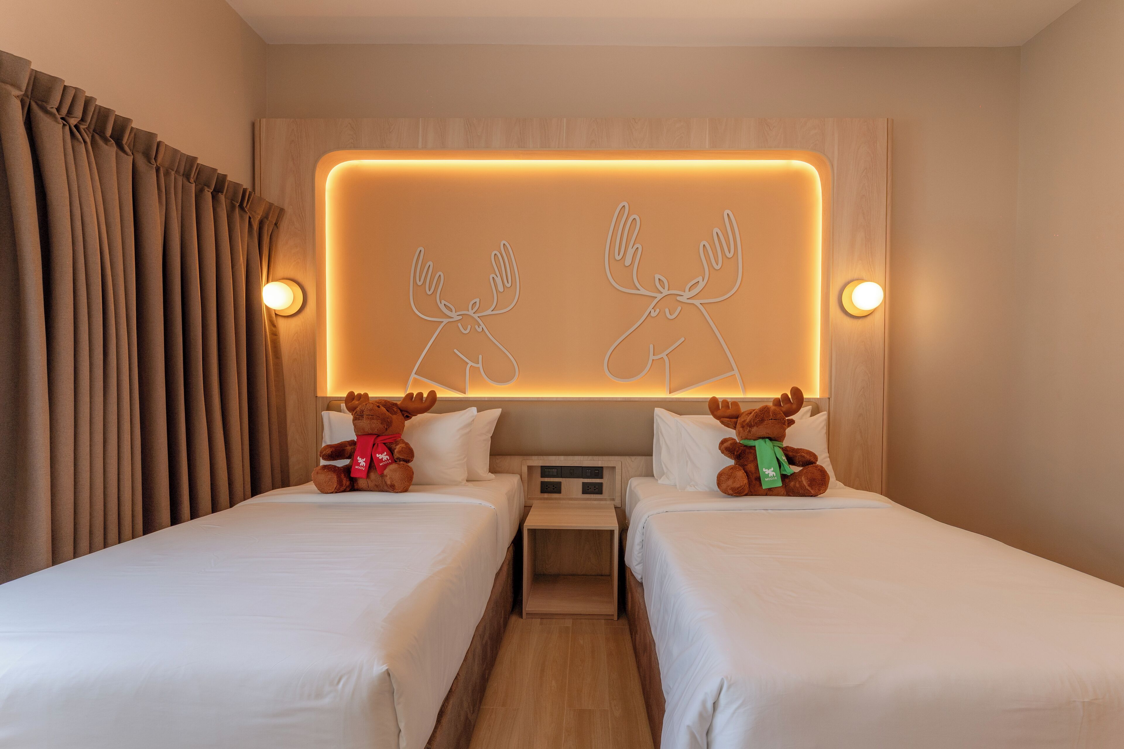 Ein Hotelzimmer mit zwei Betten, einem Nachttisch und einer Wandleuchte im Elchdesign.