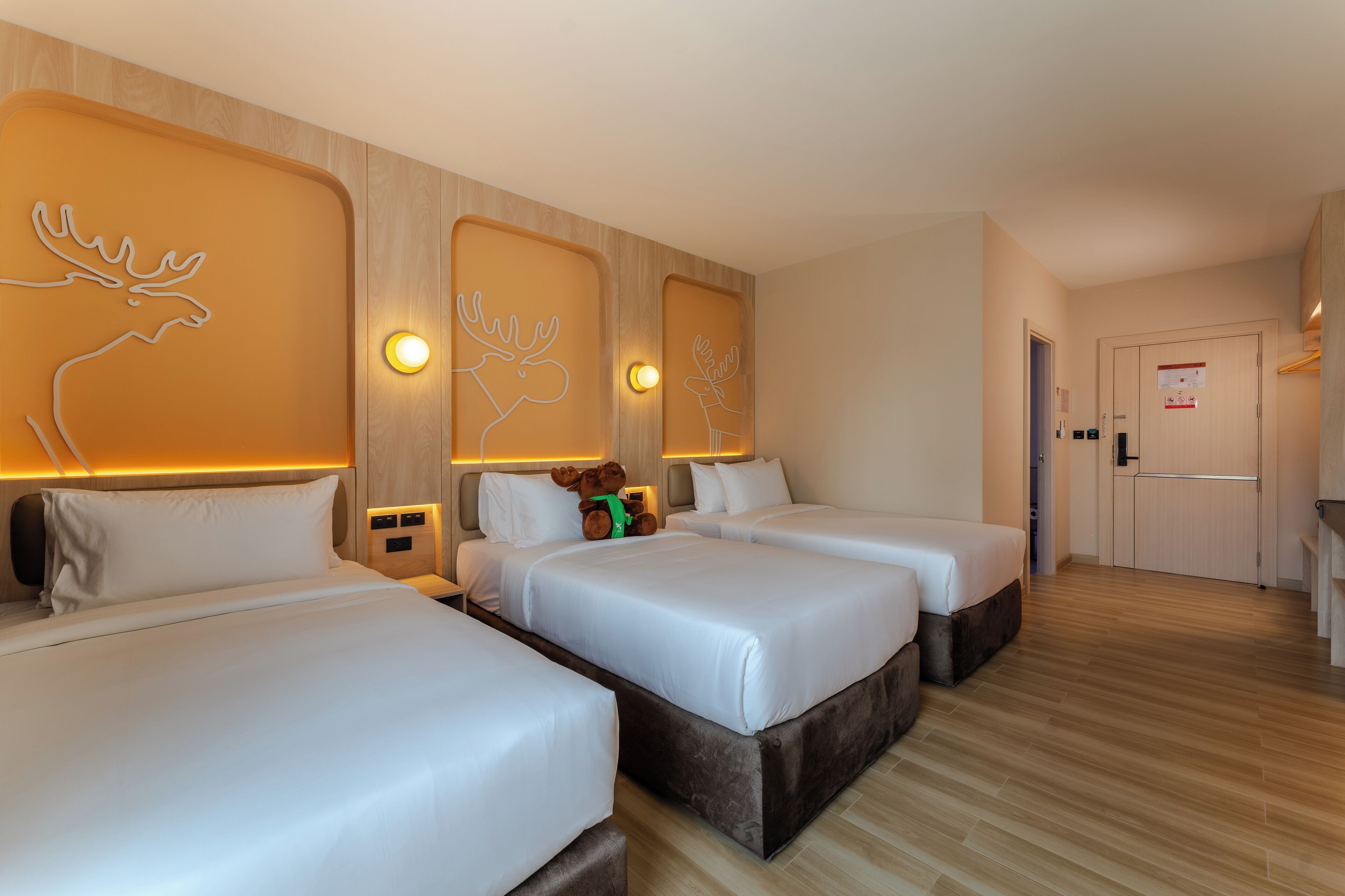 A hotel room with two beds, wooden headboards, and a small kitchenette.