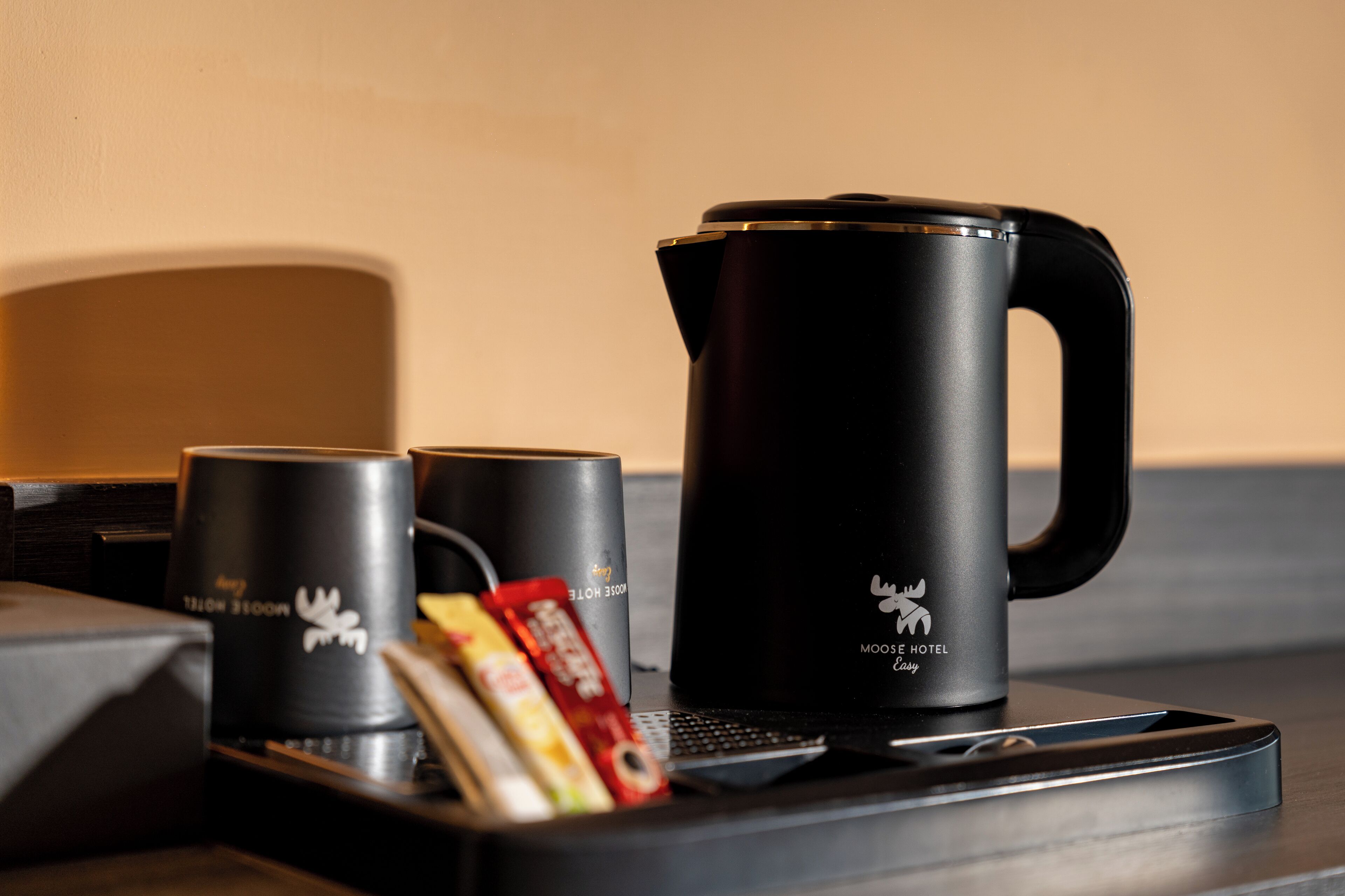 A coffee maker, two mugs, and a tray with snacks on a table.