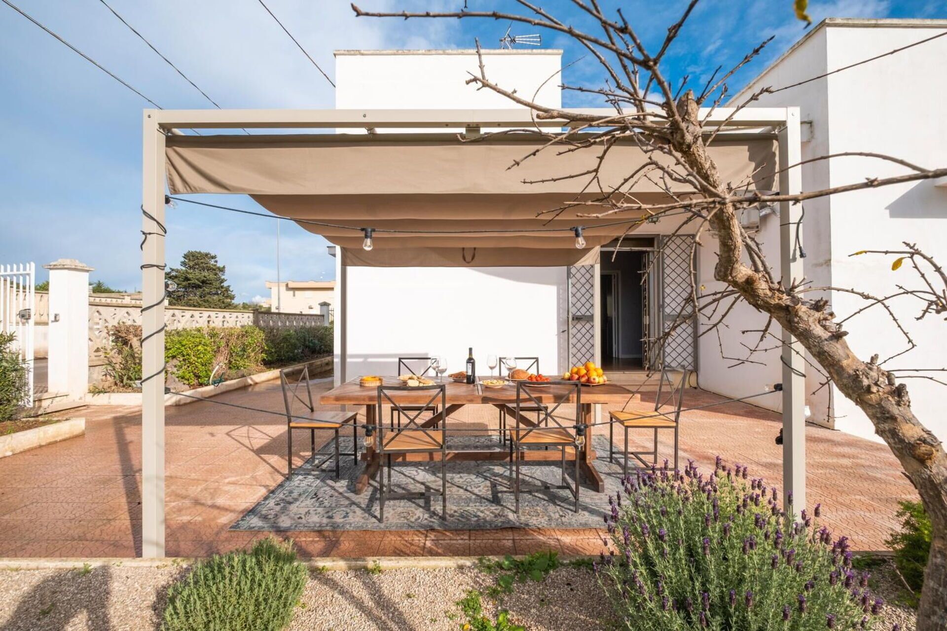Eine Terrasse im Freien mit Tisch und Stühlen, einer Pergola und Blick auf ein Gebäude im Hintergrund.