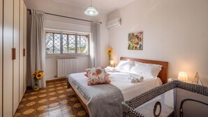 Een hotelkamer met een bed, een raam met gordijnen, een radiator, een wandairconditioner, een schilderij en een vloer met patroon.