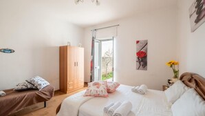 A bedroom with a bed, a wardrobe, a small table with a vase, and a door leading to a garden.