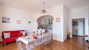 A dining area with a table set for four, a red sofa, and a kitchen in the background.