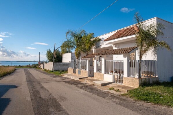 Una calle costera con casas blancas, un portón de metal y una vista despejada del mar.