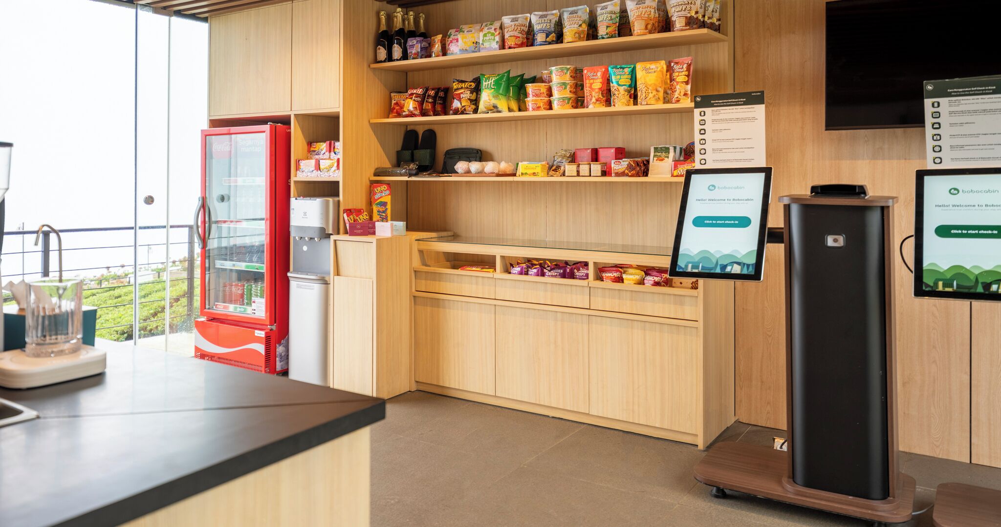 A kitchenette with a refrigerator, a microwave, a coffee machine, and shelves stocked with snacks and condiments.
