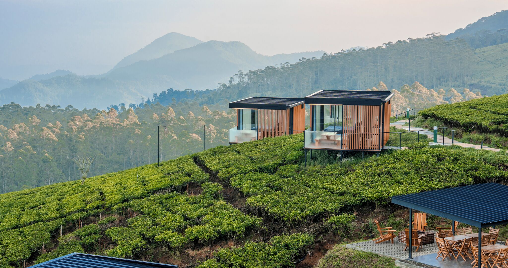 Una casa moderna con facciata in vetro, immersa in un pendio ricoperto di vegetazione lussureggiante e con montagne sullo sfondo.