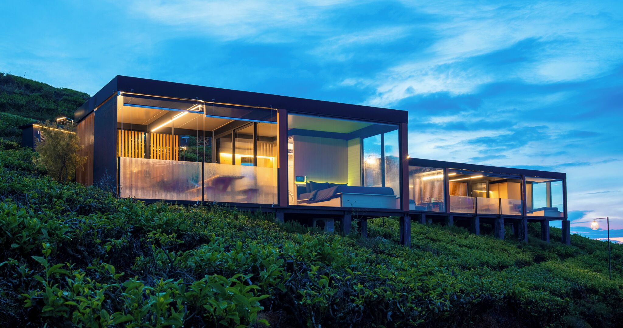 Una casa moderna de vidrio con un balcón, ubicada en una ladera.