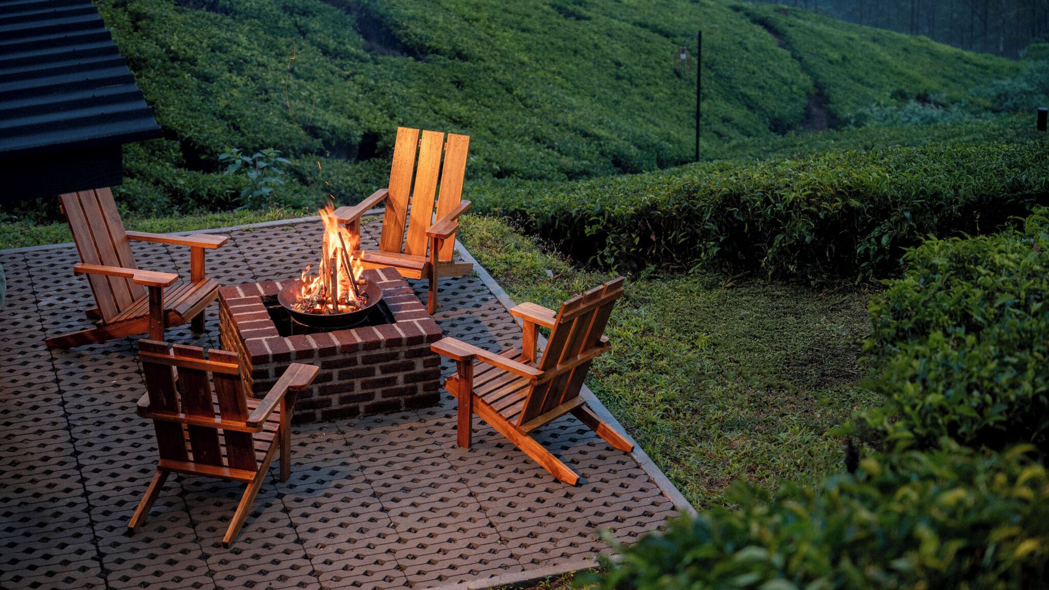 A fire pit surrounded by wooden chairs on a patio with a hilly landscape in the background.