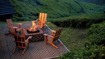 A fire pit surrounded by wooden chairs on a patio with a hilly landscape in the background.