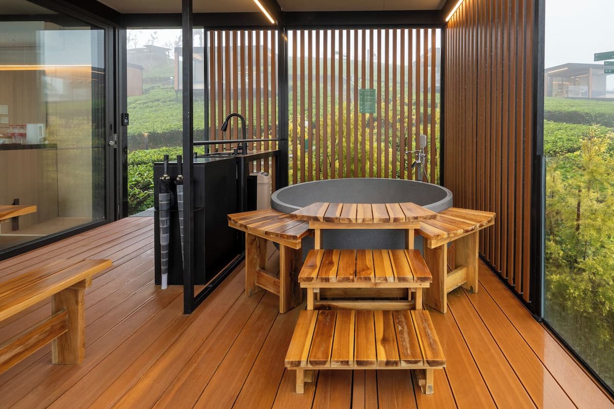 Un patio moderno al aire libre con muebles de madera, un jacuzzi y vistas a un jardín exuberante.