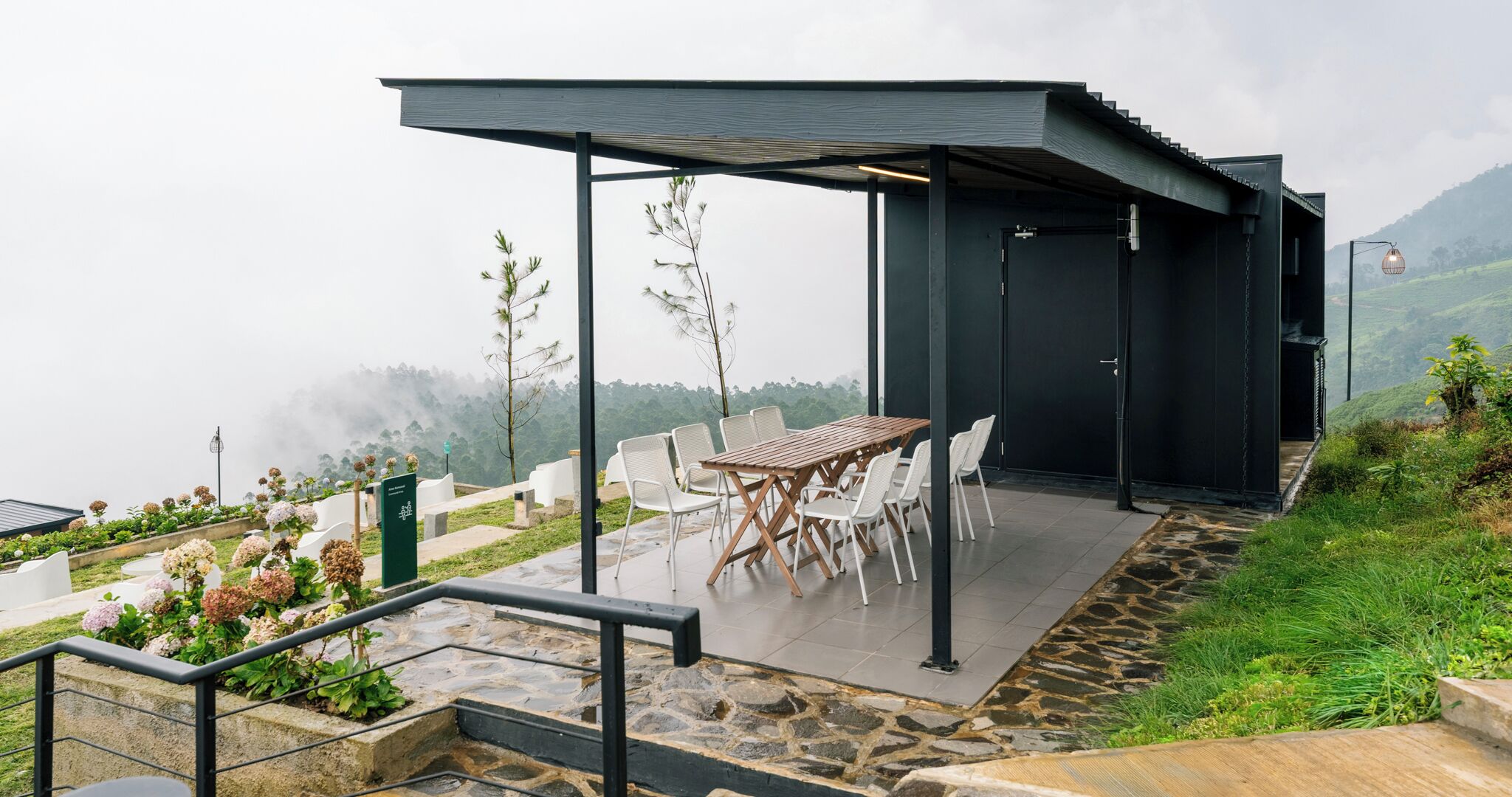 A modern outdoor seating area with a table and chairs, surrounded by a stone pathway and greenery.