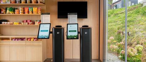 Un kiosque en libre-service doté d’un écran tactile et d’un menu numérique, situé dans un bâtiment moderne avec un revêtement mural en bois et offrant une vue sur un espace paysager aménagé.