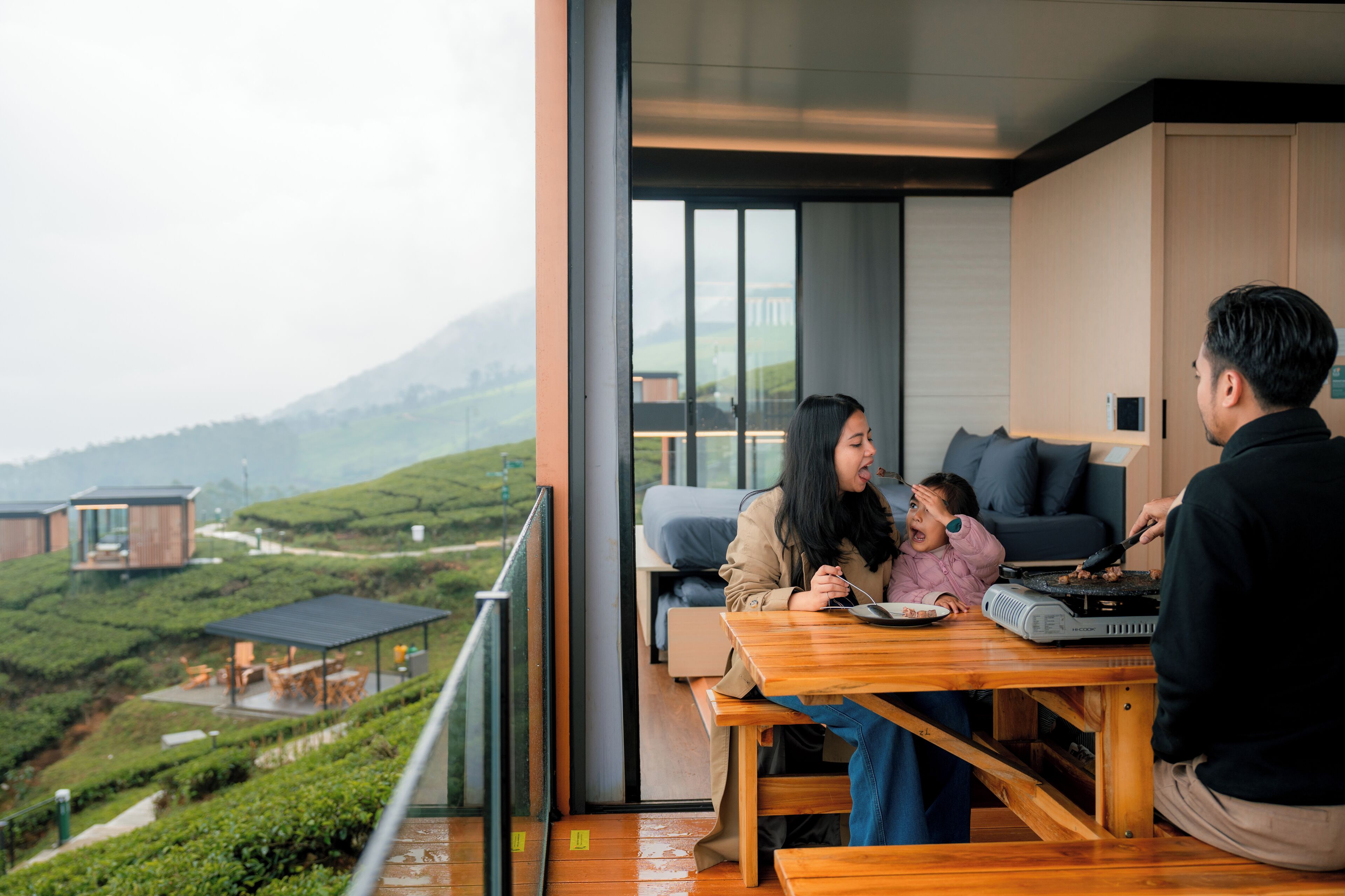 Una familia cenando en una mesa con vistas a campos de té y montañas.