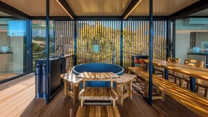 Eine moderne Terrasse im Freien mit Holztisch und -stühlen, einem Whirlpool und einer Glaskonstruktion.