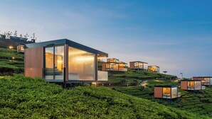 Ein modernes Anwesen an einem Hang mit mehreren Glasbungalows, jedes mit sichtbarem Innenraum und Beleuchtung.