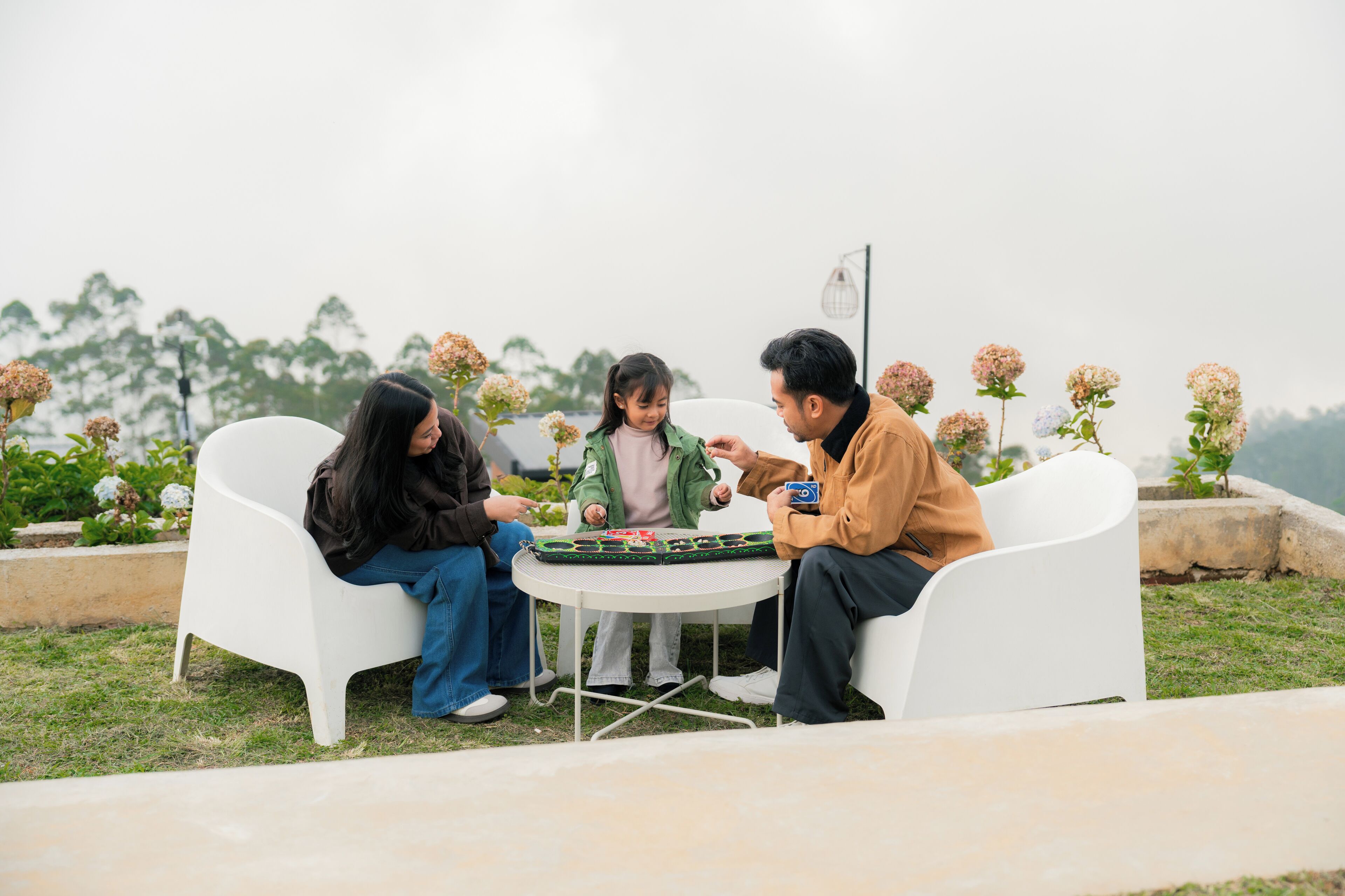 Three people seated around a small round table outdoors with a garden view.