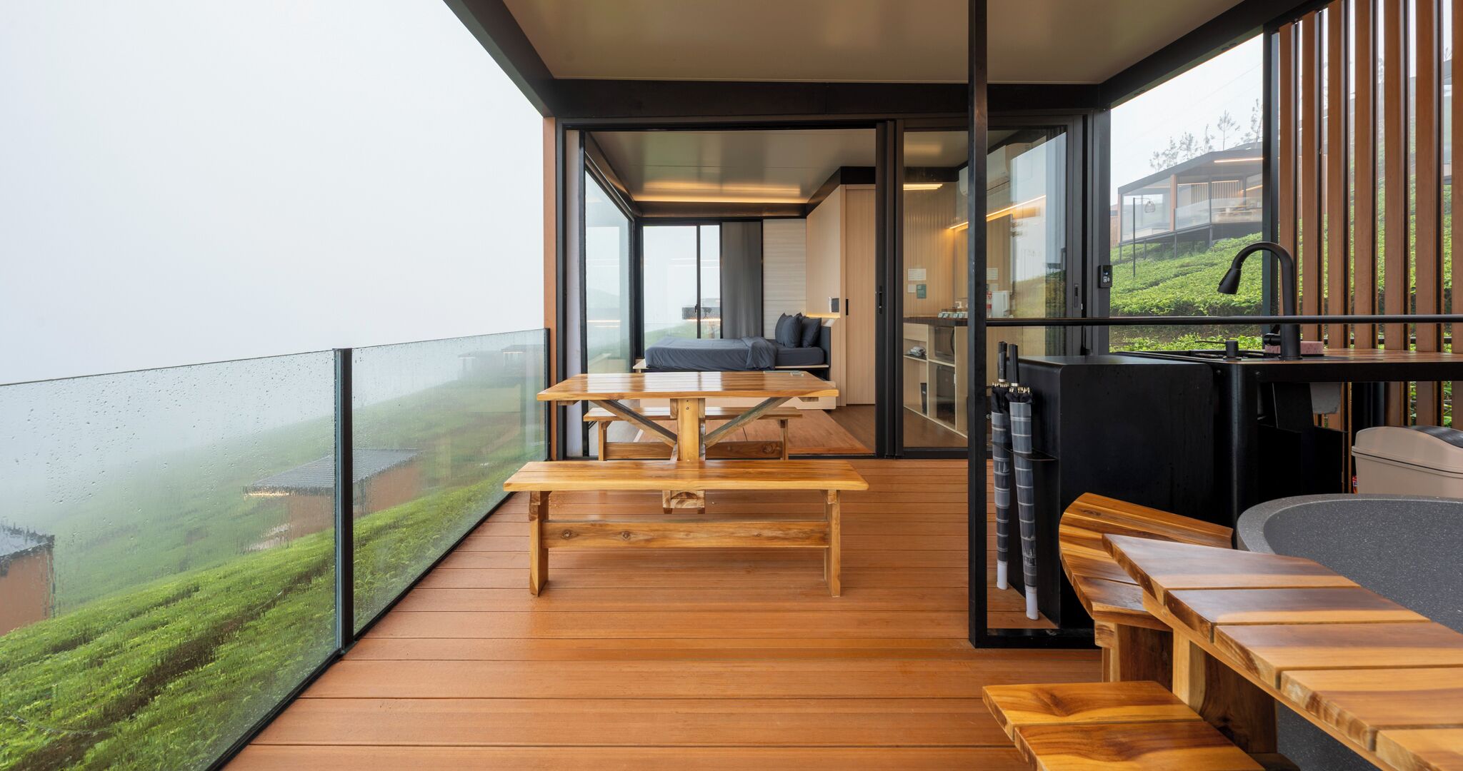 A modern balcony with wooden flooring, a wooden table, and benches.