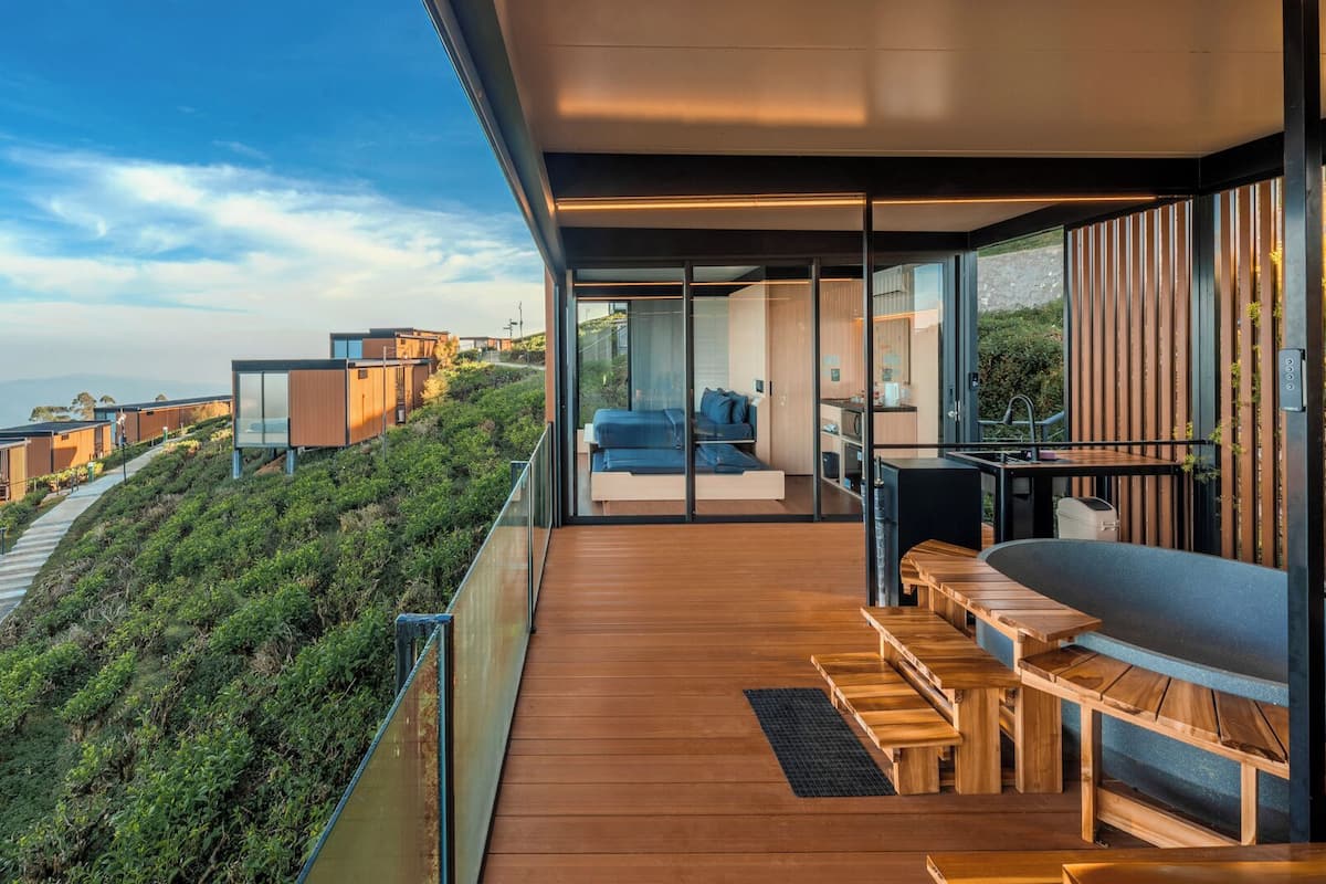 Una terraza moderna al aire libre con suelo de madera, una zona de estar y vistas a una colina con edificios.