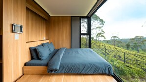 Ein modernes Schlafzimmer mit einem großen Bett, Holzwänden und Blick auf eine grüne Landschaft durch ein großes Fenster.