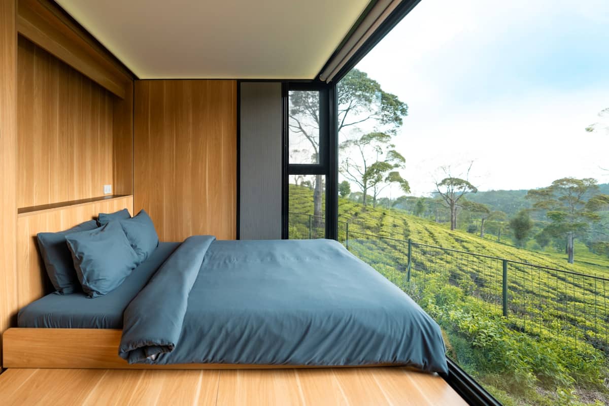 Un dormitorio moderno con una cama grande, paredes de madera y vistas a un paisaje verde a través de un ventanal amplio.
