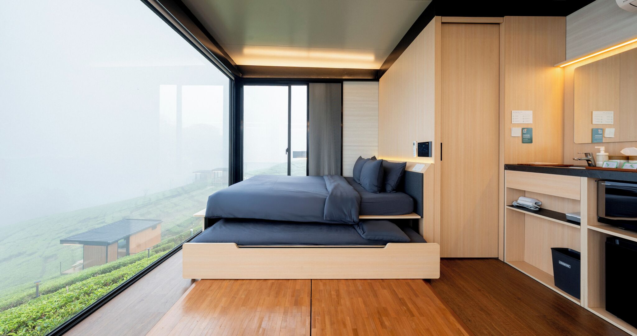 A modern bedroom with a built-in bed, a small kitchen area, and a view of the city.