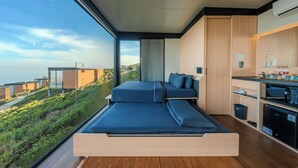 Ein modernes Schlafzimmer mit einem großen Bett, einer Küchenzeile und Blick auf eine Hügelterrasse.