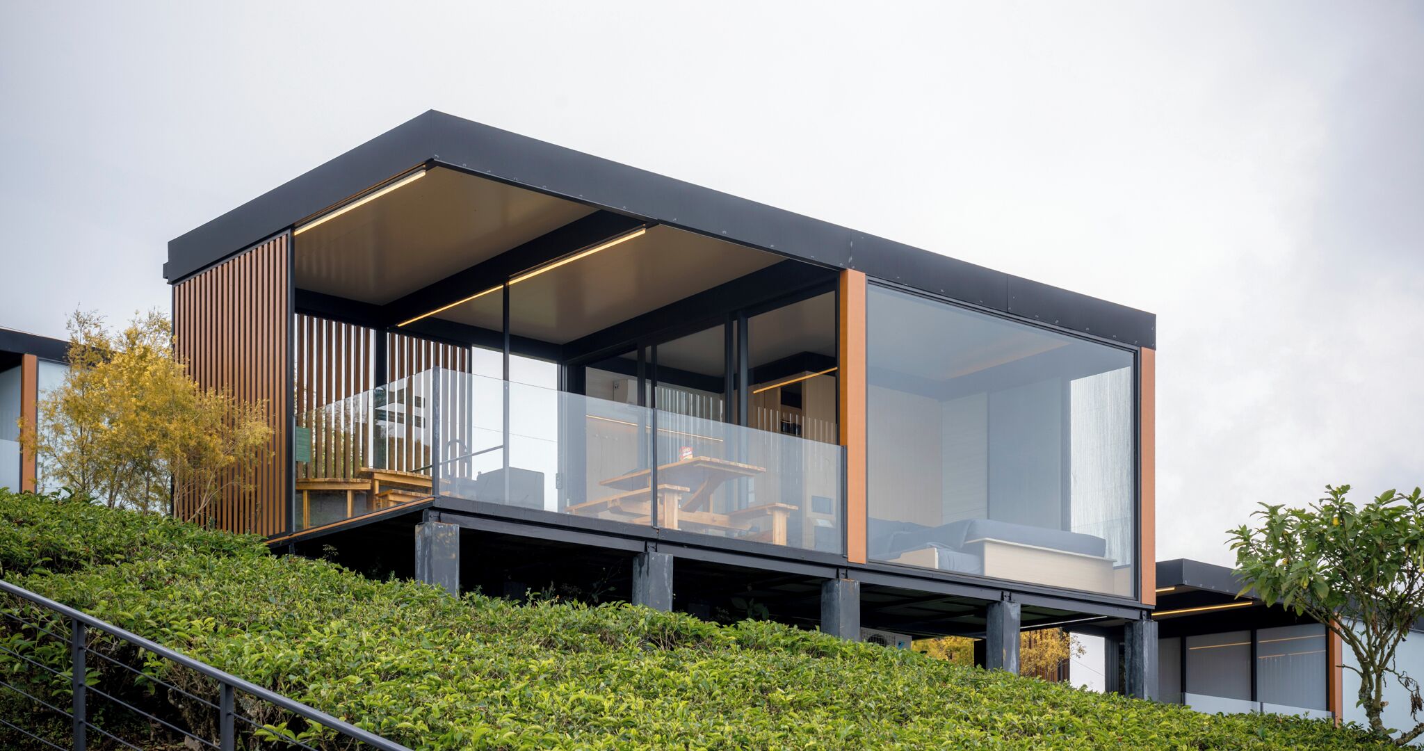 A modern house with large glass windows, a wooden deck, and a staircase leading to the entrance.