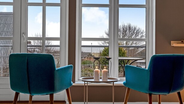 A room with two teal chairs facing a large window with a view of a body of water and buildings.