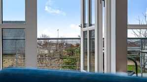 A room with a large window overlooking a residential area, a metal railing, and a view of houses and trees.