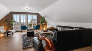 A modern loft apartment with a black leather sofa, a white armchair, and a dining area with blue chairs.