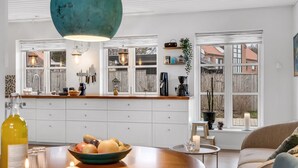 A modern kitchen with white cabinets, a wooden countertop, and a large window. There is a bowl of fruit on the counter and a bottle of olive oil.