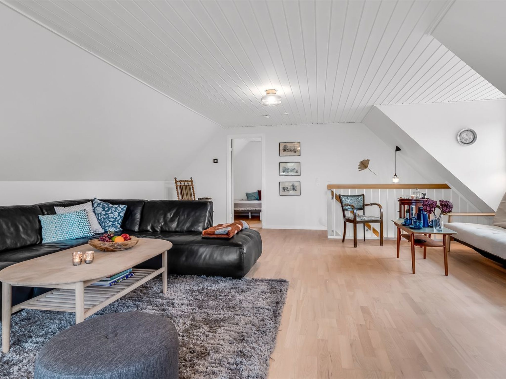 Un loft moderno con techo alto, un sofá de cuero negro, una mesa de comedor de madera y una escalera que lleva a un nivel superior.