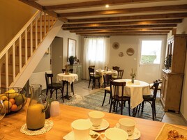 Un comedor con mesas y sillas de madera, una escalera y vistas al exterior.